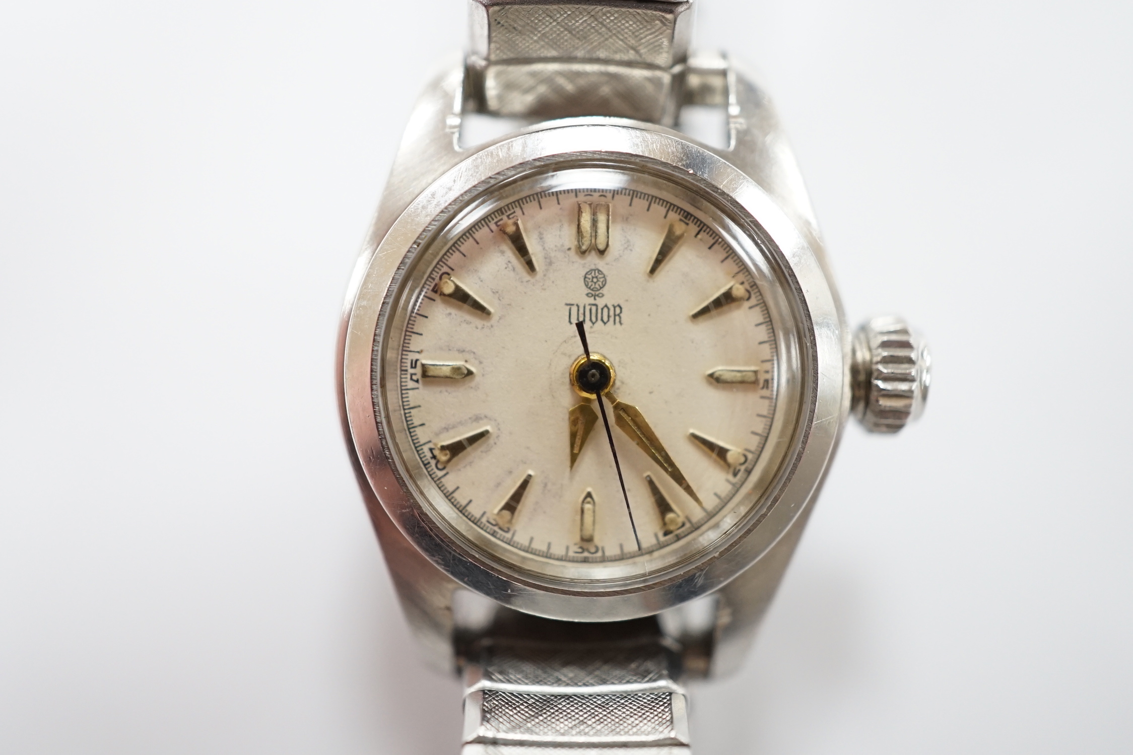 A lady's stainless steel Tudor manual wind wrist watch, with baton numerals, on an associated flexible bracelet.